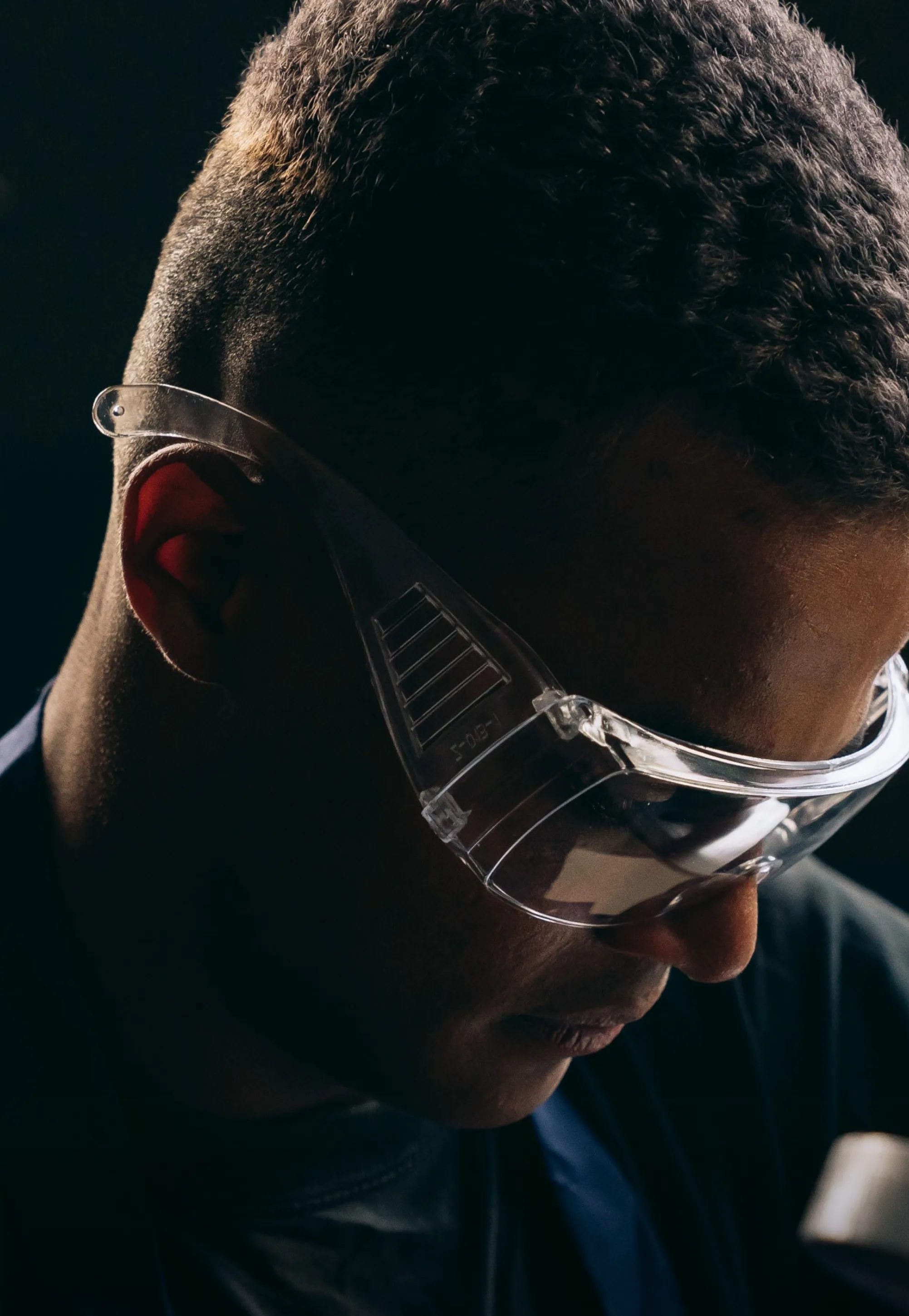 A close-up portrait of an engineer wearing goggles against a dark background.
